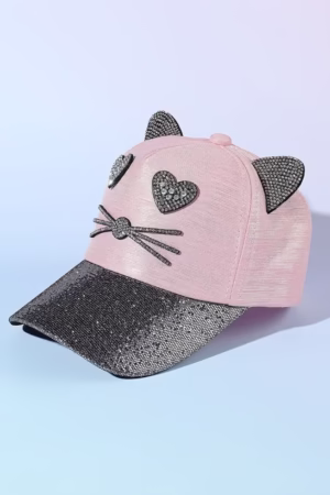 A pink cap with glittery rhinestone cat ears, heart-shaped eyes, whiskers, and a sparkling black visor, displayed on a soft gradient background.
