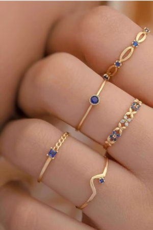 A set of delicate gold rings featuring blue sapphire-like stones and intricate designs, ideal for stylish stacking.