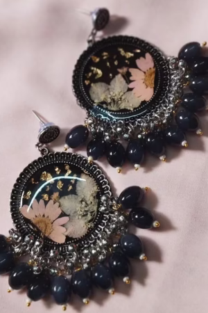 A pair of circular earrings with pressed flowers inside resin, adorned with black and silver beads.