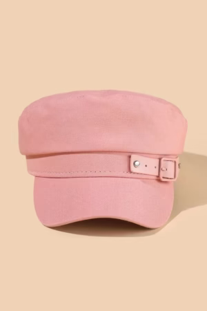 A pink cadet-style cap with an adjustable strap and metallic details, displayed against a beige background.