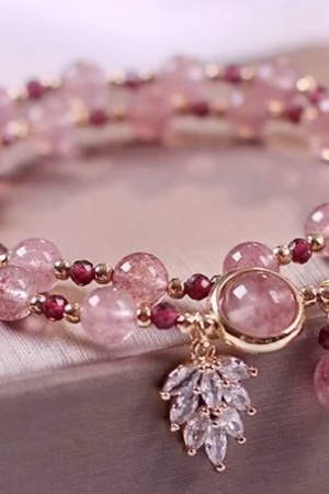 A stylish bracelet with pink gemstone beads, golden spacers, red accents, and crystal charm details.