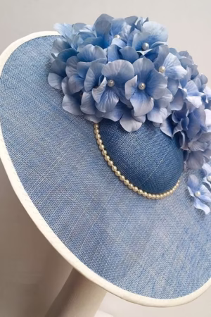 Stylish blue straw hat featuring delicate hydrangea floral accents and pearl embellishments, ideal for summer outings and adding a touch of elegance to your look.