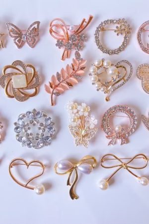 A collection of decorative hijab pins with floral, butterfly, bow, and heart designs, embellished with pearls and crystals.