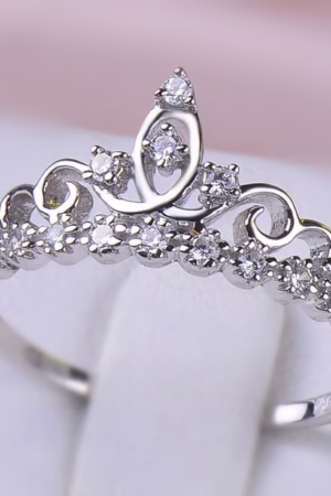 Silver tiara-shaped ring adorned with sparkling crystals, displayed on a soft surface.