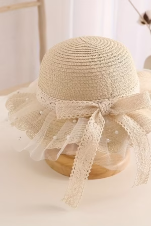 A beige straw hat with lace trim, pearl embellishments, and a decorative bow, placed on a wooden display.